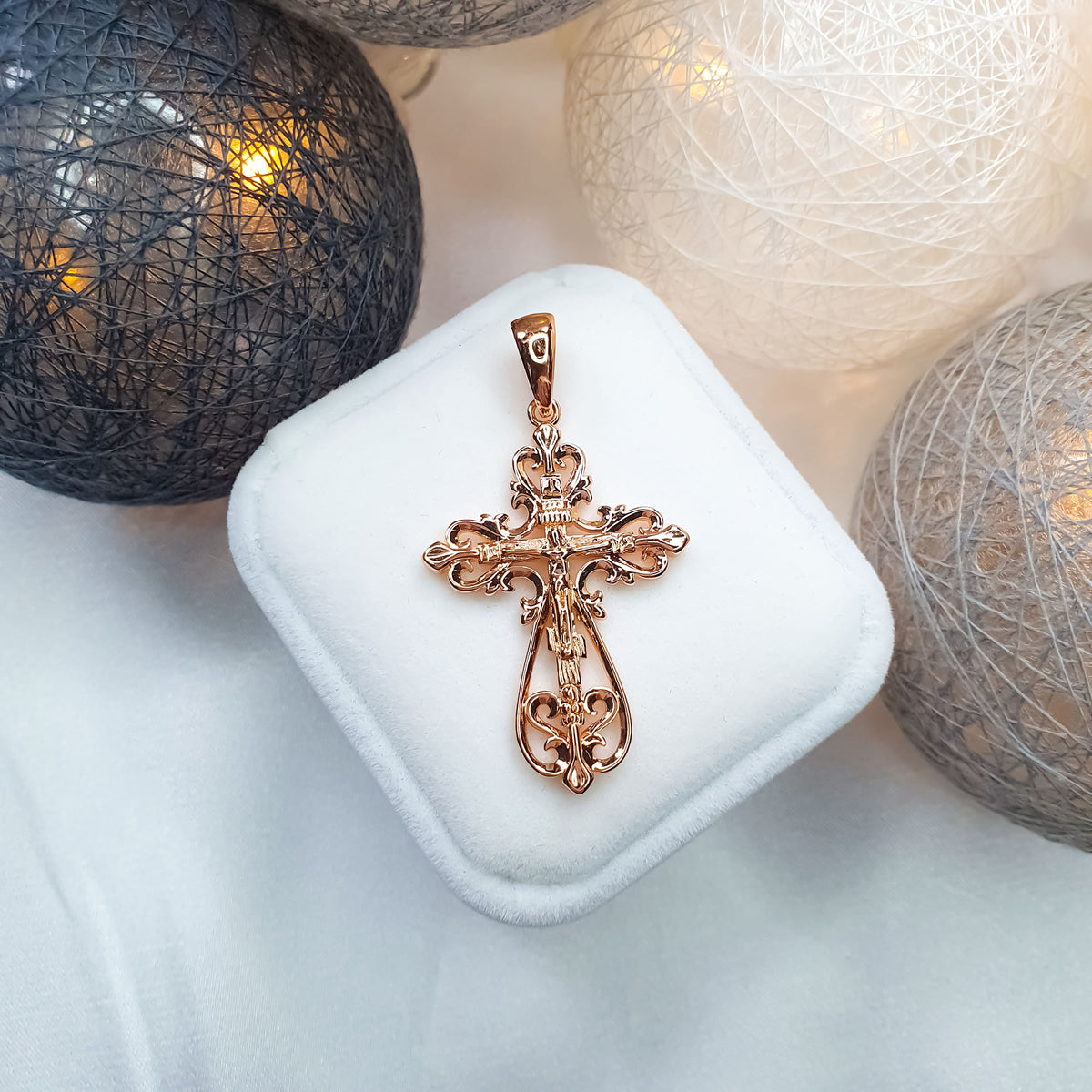 Openwork cross pendant on a white velvet box among glittering baubles