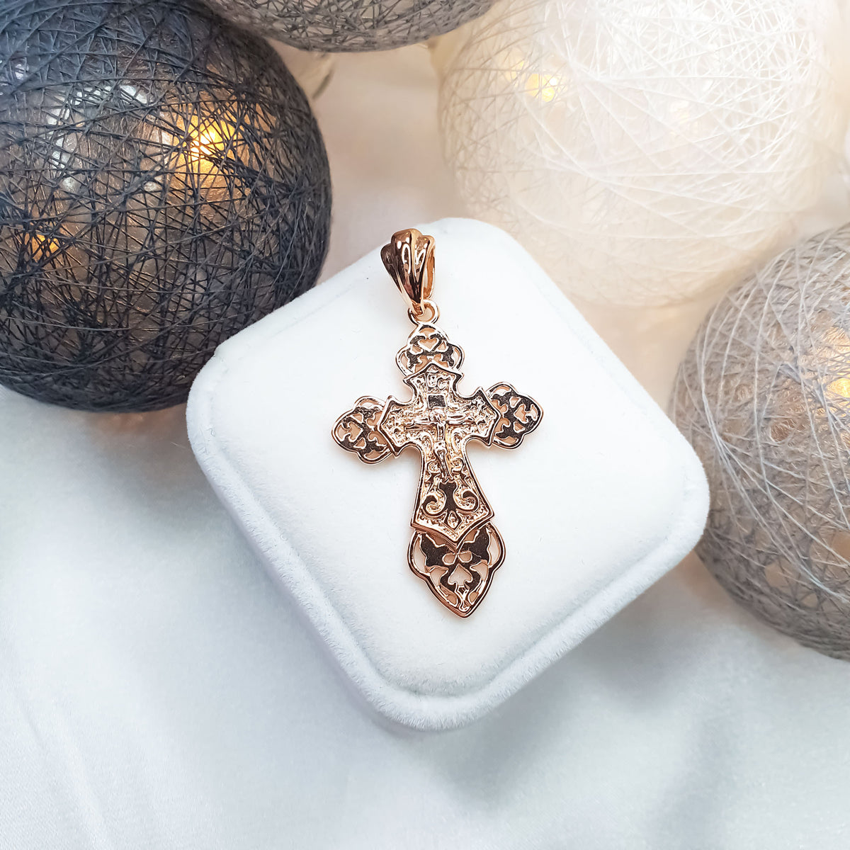 Gold-plated Orthodox cross on a white velvet case among glowing baubles