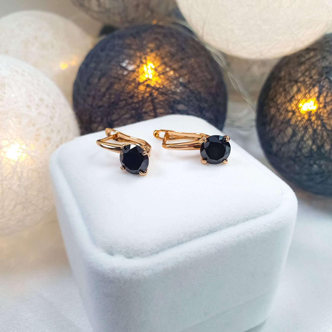 Black cubic zirconia earrings on a white gift box among sparkling decorative lights