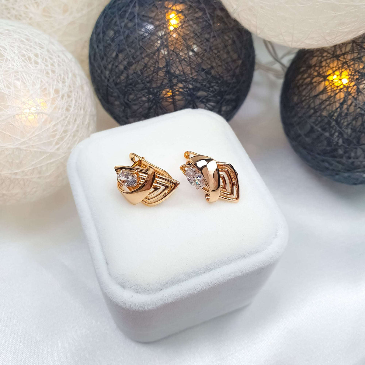 Pair of oval cubic zirconia earrings with openwork lines on a white velvet box