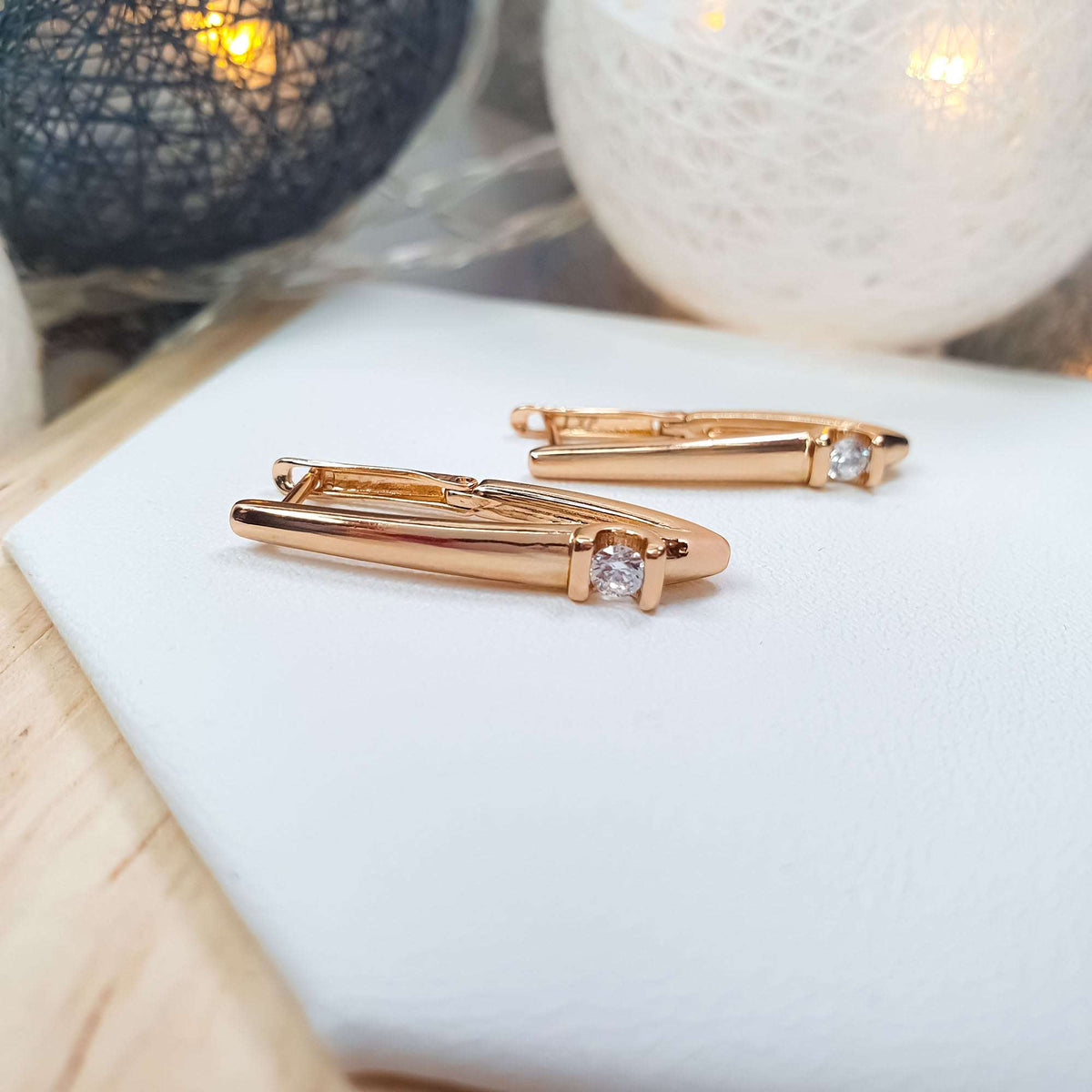 Close-up of gold-plated V-shaped earrings on a white stand, sparkling cubic zirconia