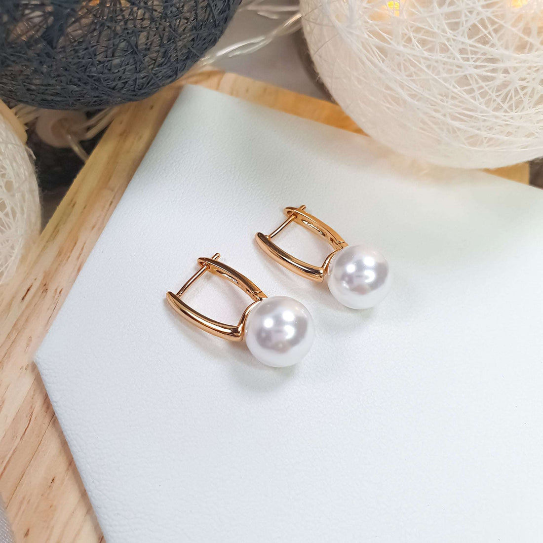 Gold-tone pearl earrings at an angle on a light surface, warm lights