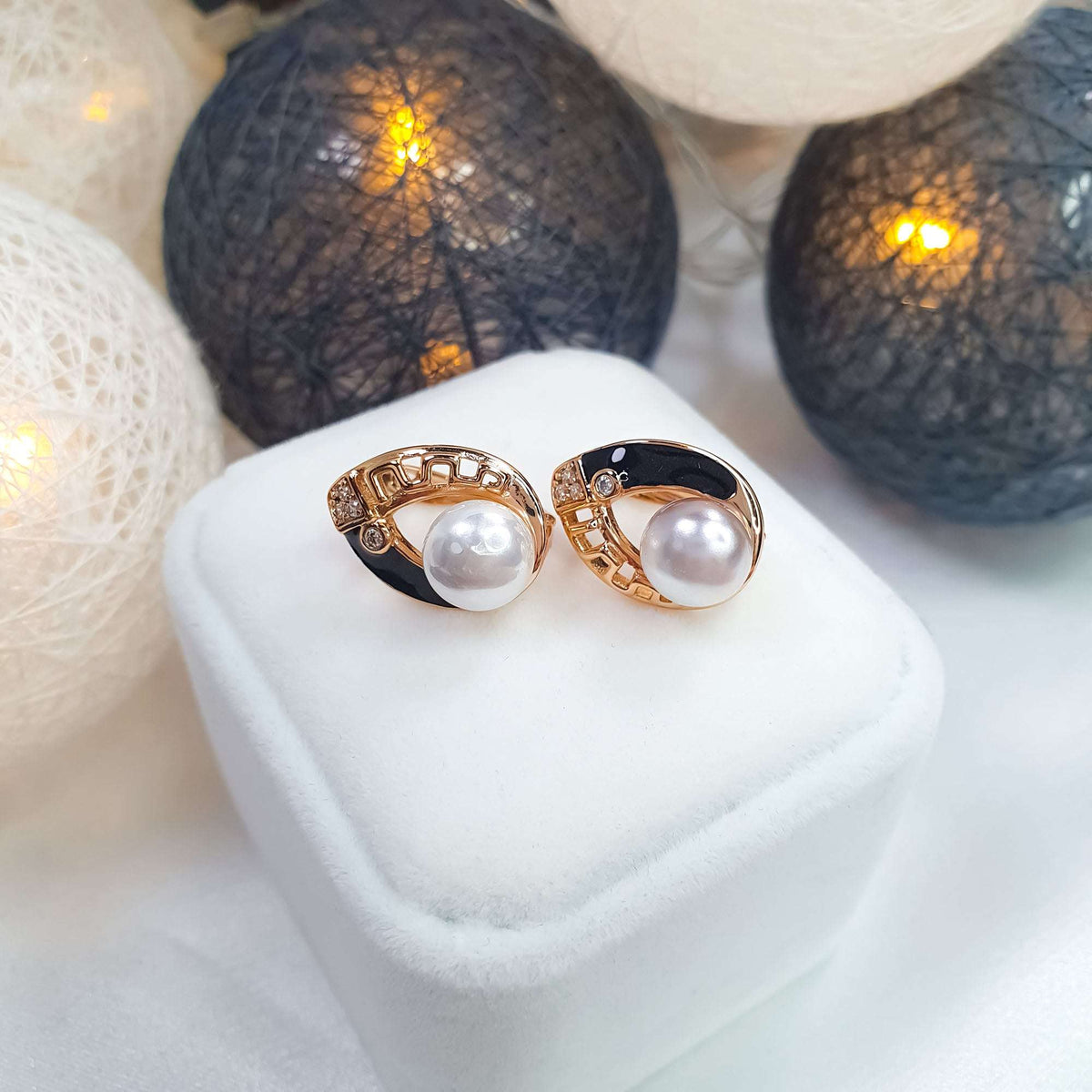 Pearl earrings on a white box, close-up of openwork gold-tone pattern and black enamel