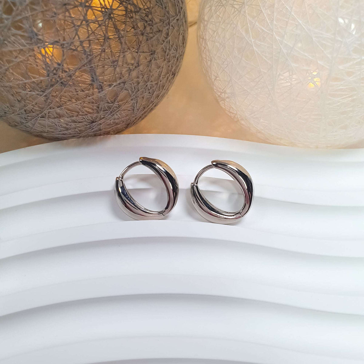 Pair of shiny silver-tone hoop earrings on a white wavy stand