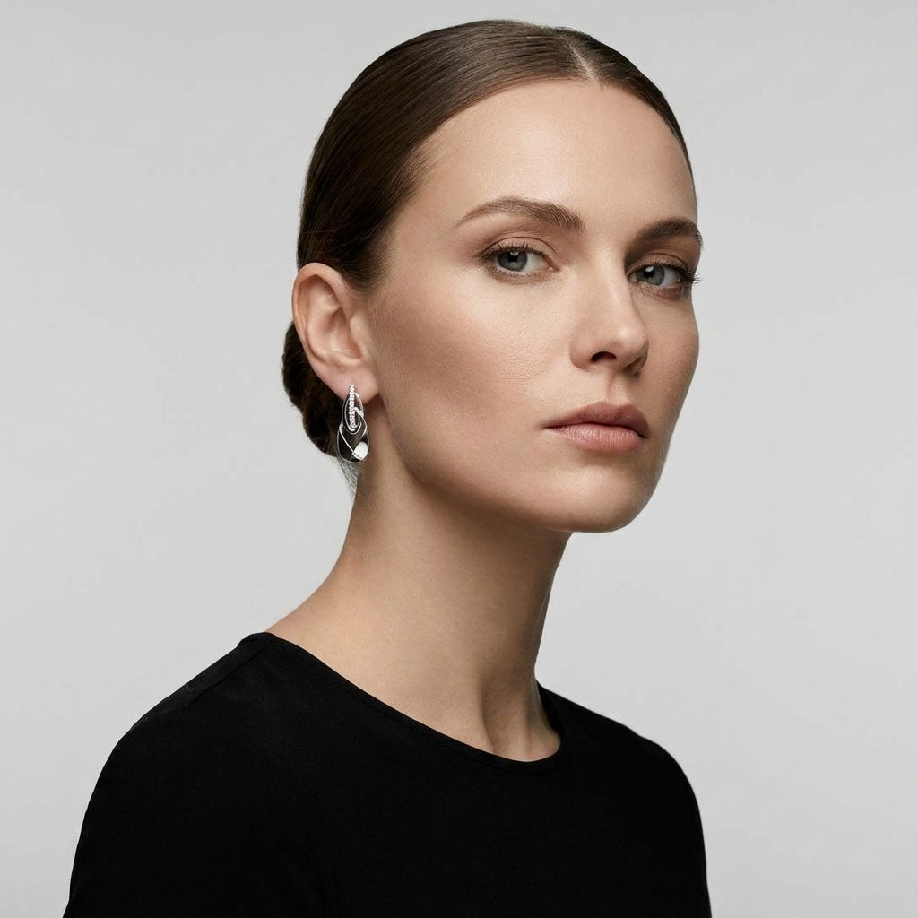 Silver-tone teardrop earring on a woman's ear against a grey background