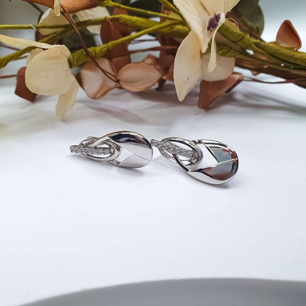 Two silver-tone earrings with twisted loops and a row of zirconia on white