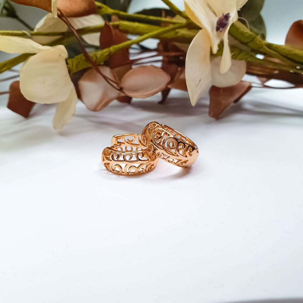 Two gold-plated earrings with openwork spirals on a light surface near flowers