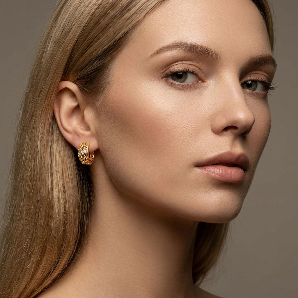 Wide gold-plated hoop earring in a woman's ear, openwork pattern and stones close up