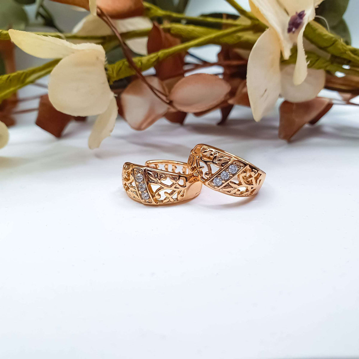 Pair of openwork hoop earrings on a light surface with dried flowers
