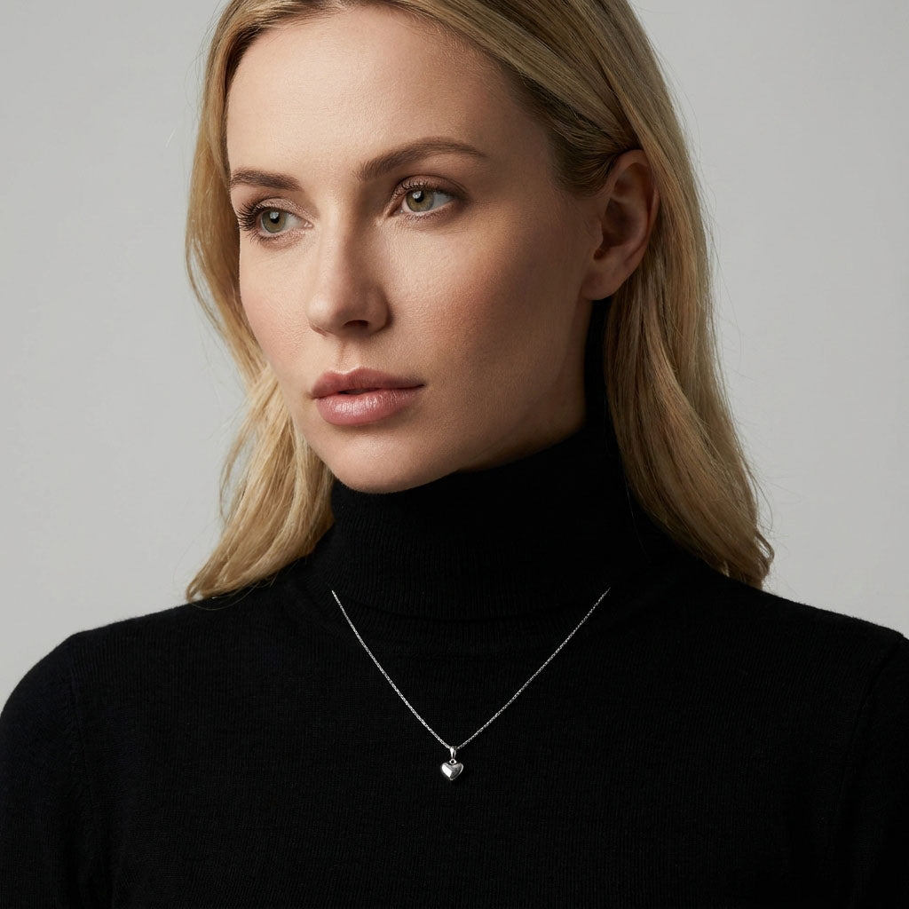 Model in a black polo neck wearing a small silver-tone heart pendant