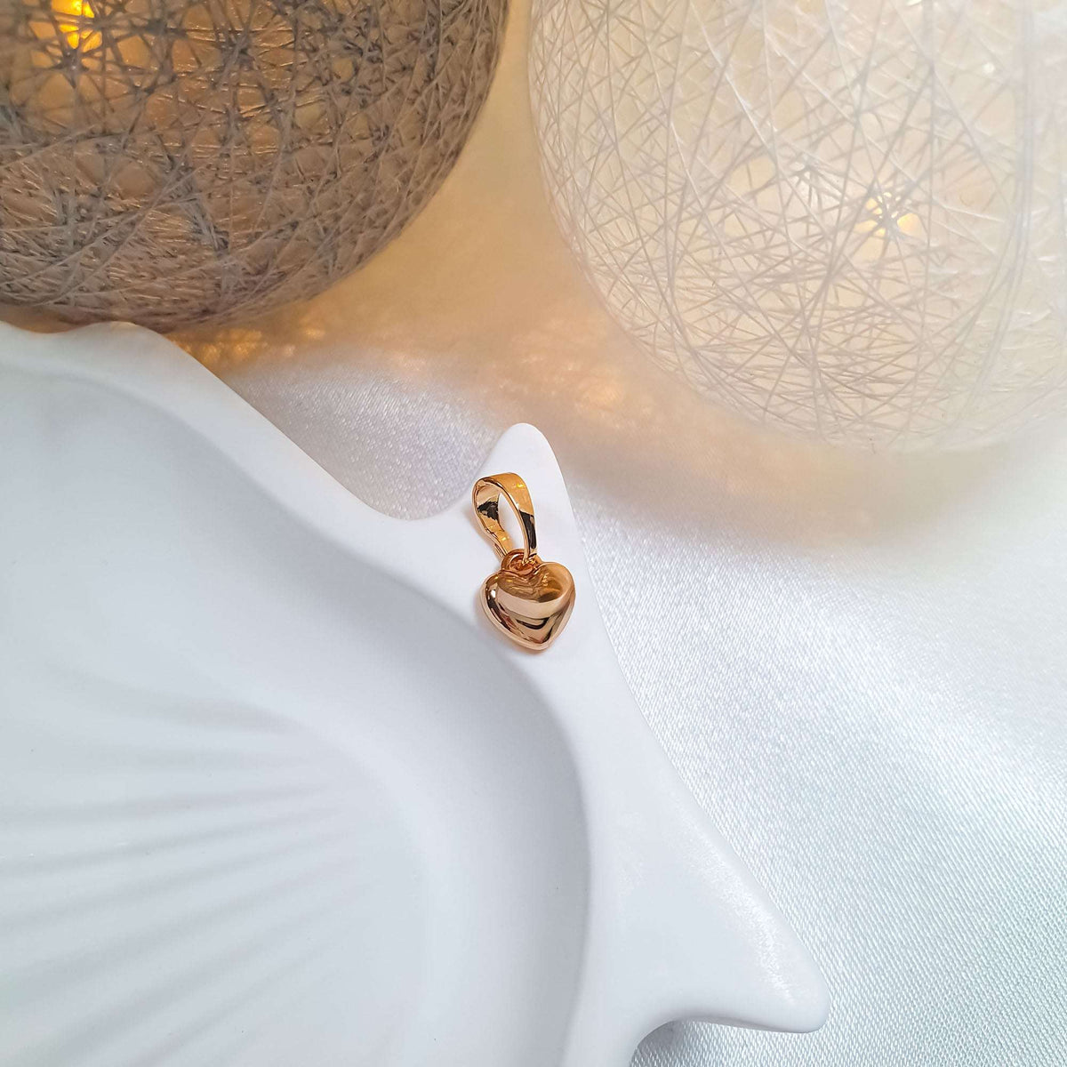 Gold-plated heart pendant close up on a light ceramic stand