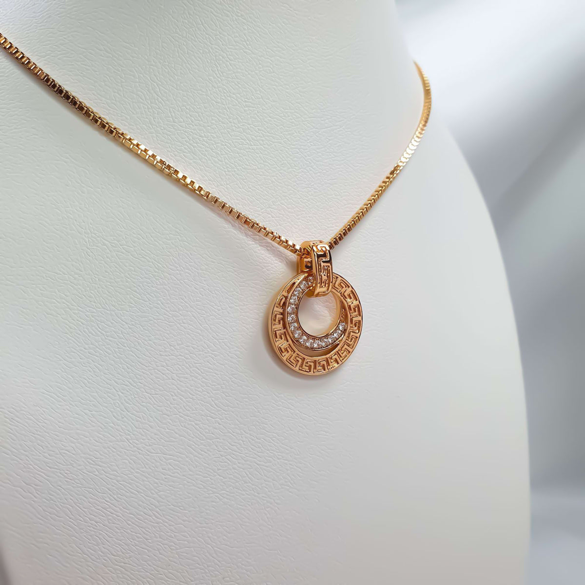 Close-up of gold-tone circles with a meander pattern and white cubic zirconia