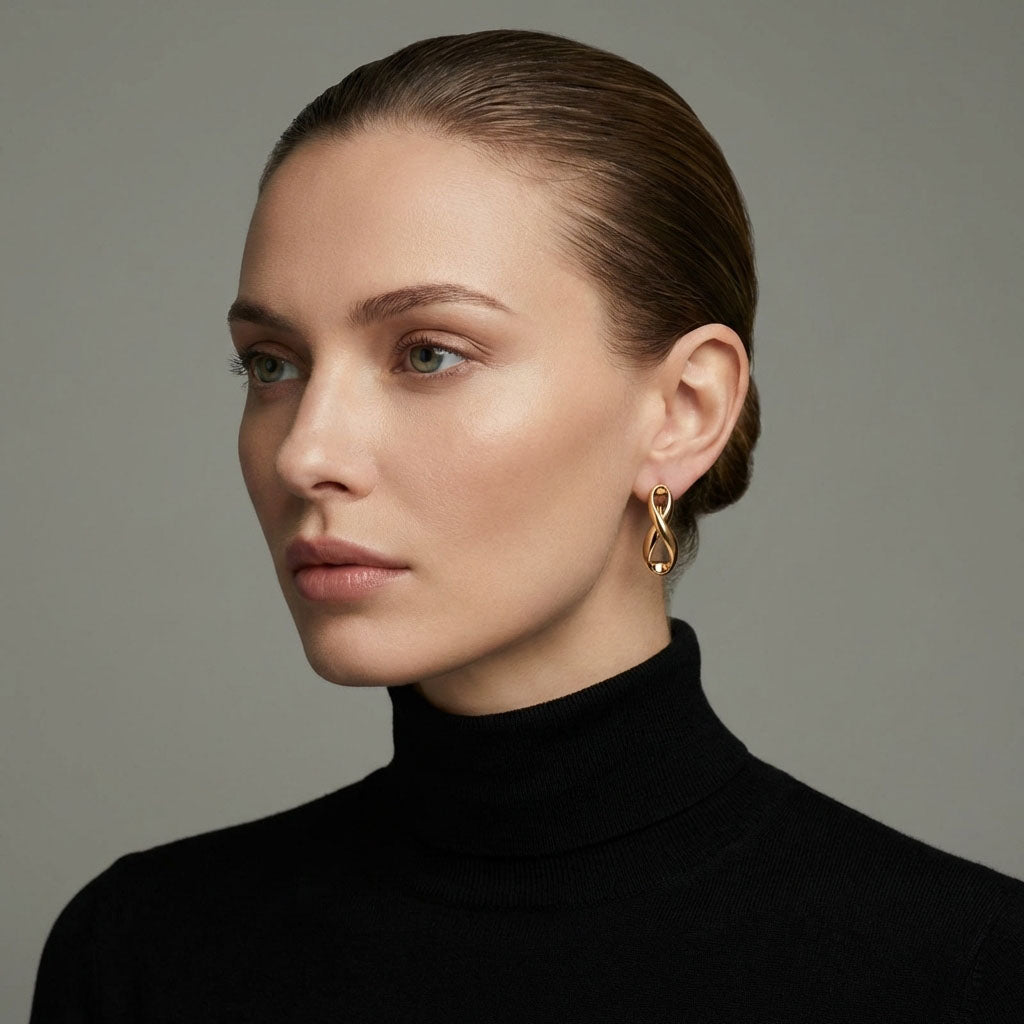 Model in a black polo neck wearing a gold-plated infinity earring, grey background