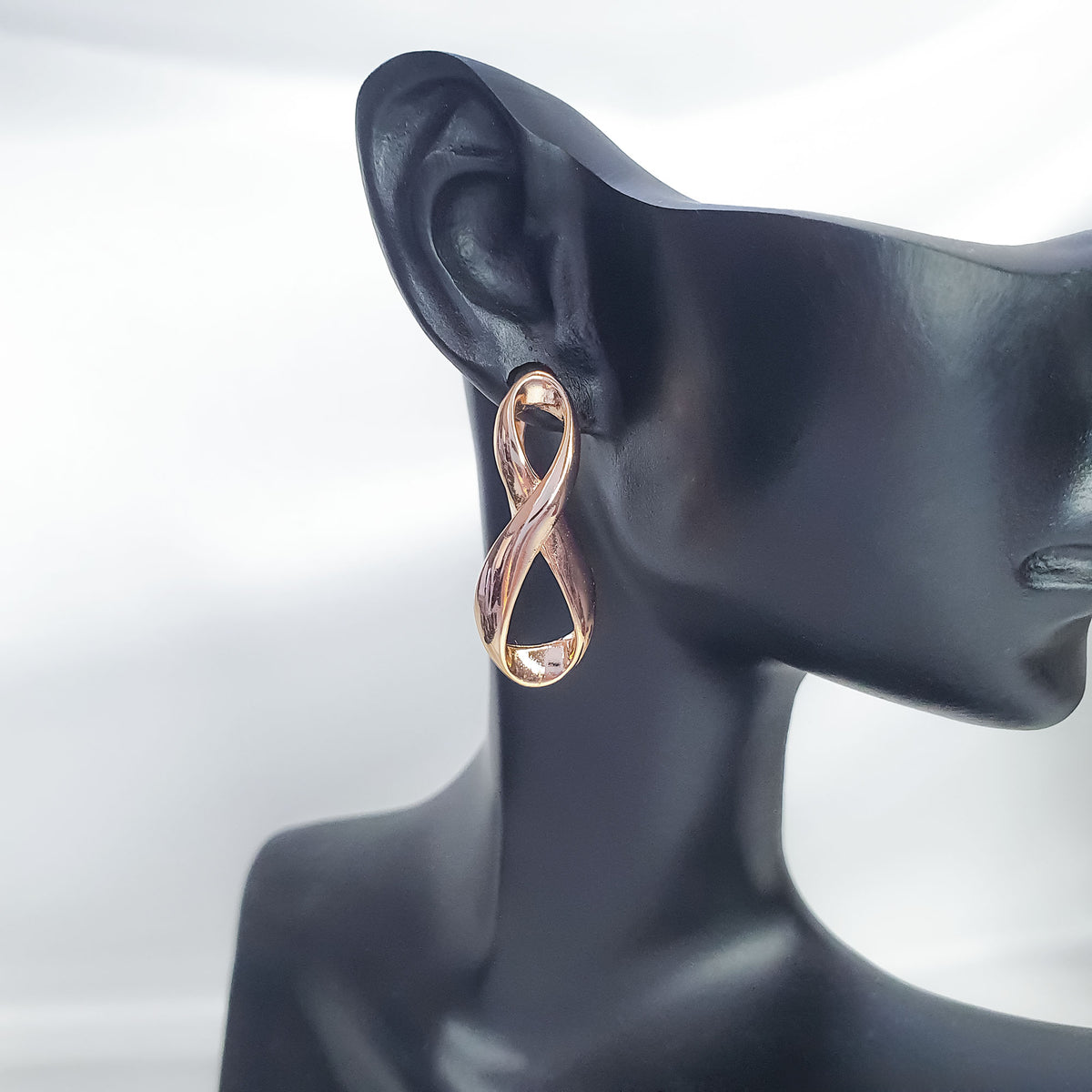 Gold-plated infinity earring on a black mannequin ear showing its curved, glossy shape