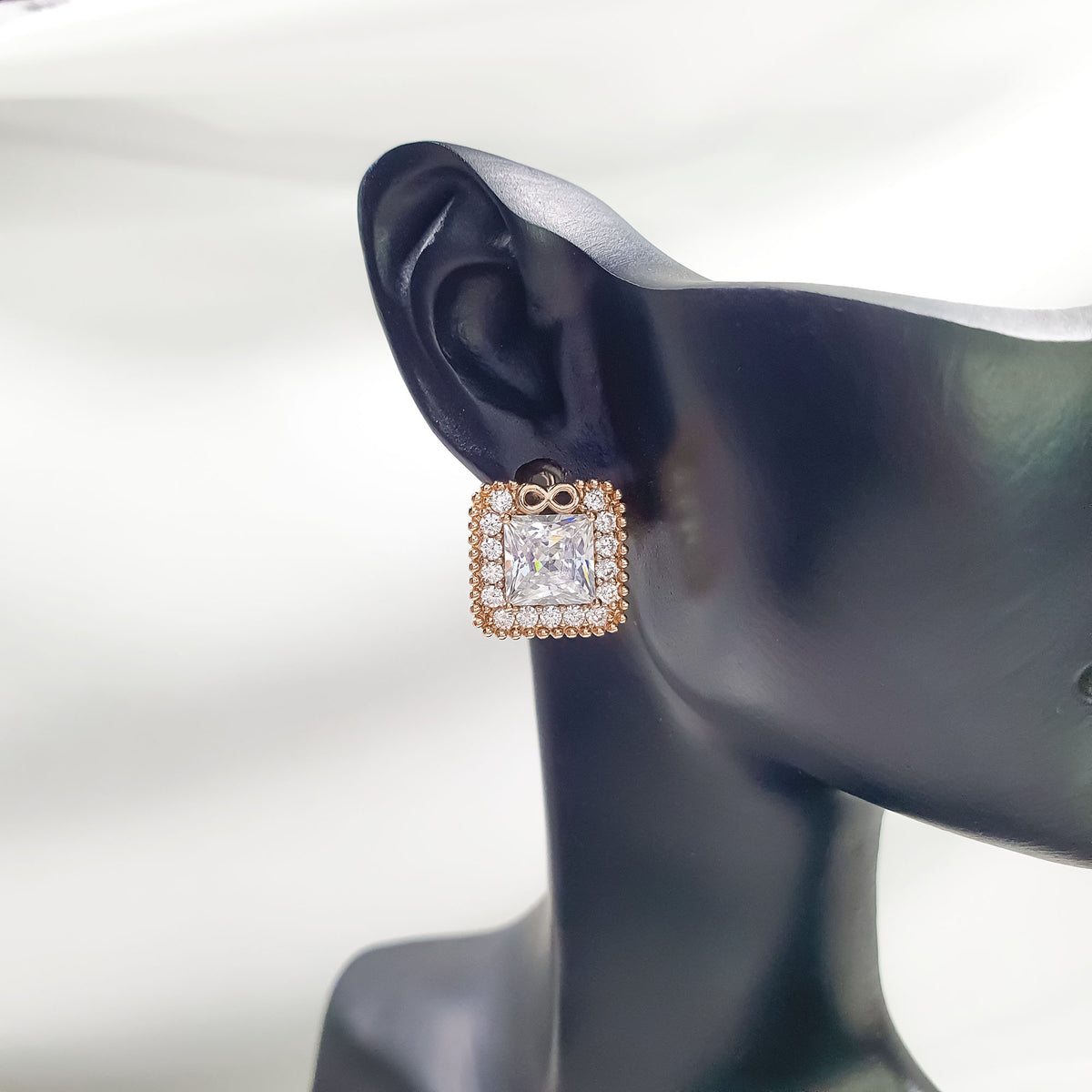 Square earring with rose gold-tone edge and infinity sign on a dark ear model