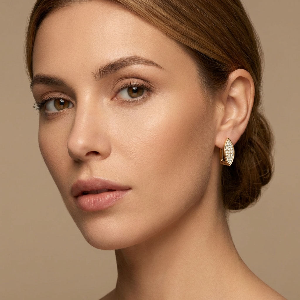 Model with hair pulled back wearing gold-plated leaf earrings, beige background