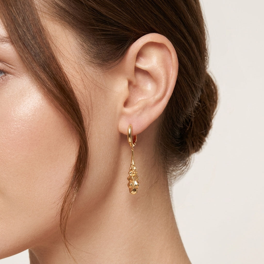 Model wearing a long gold-plated earring swinging beside the ear, close-up