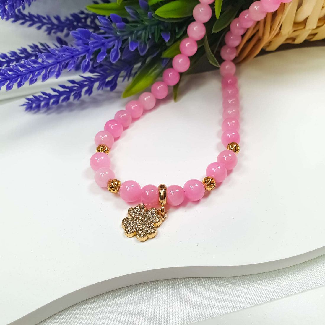 Soft pink jadeite necklace with a clover charm beside flowers