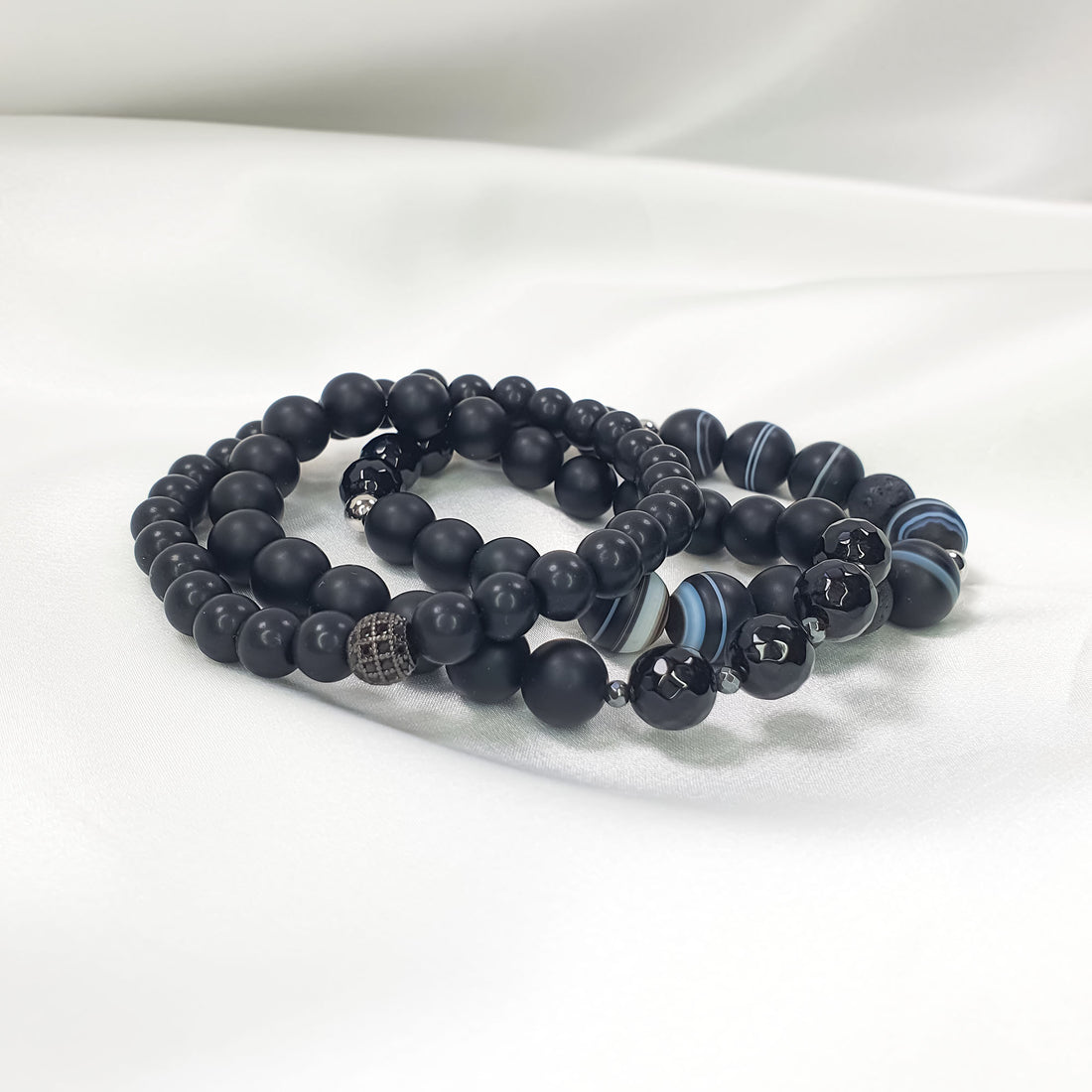 Black bracelet set on white satin, side view showing different bead textures