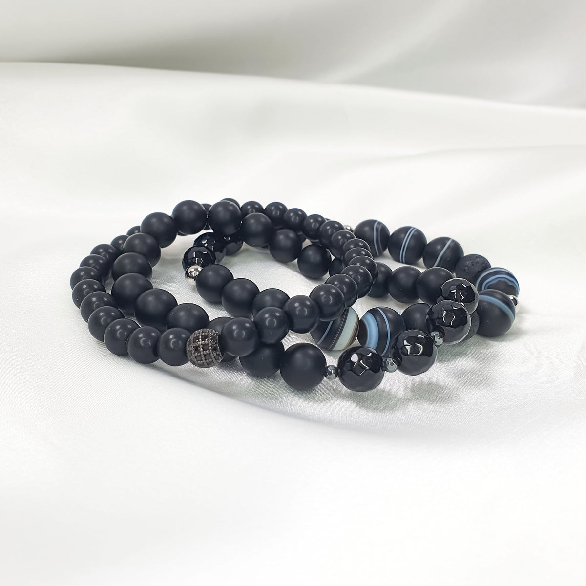 Black bracelet set on white satin, side view showing different bead textures