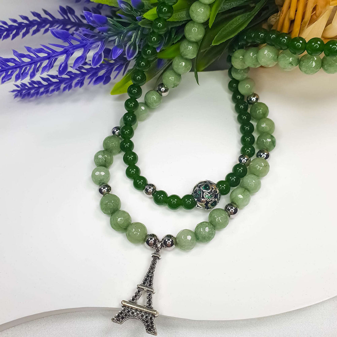 Green bead necklace with a decorative ball and tower pendant beside lavender