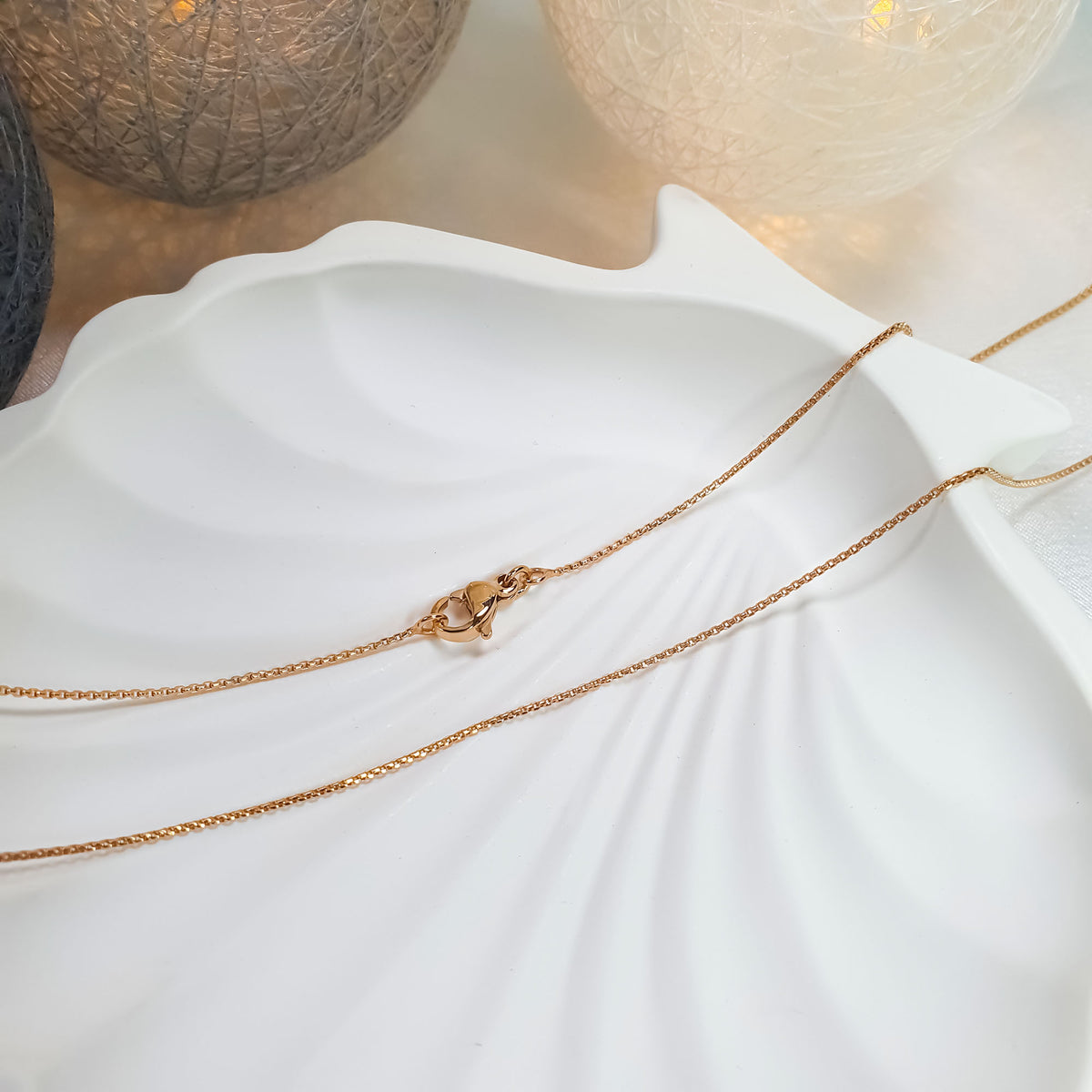 Long gold-tone chain on a white shell-shaped tray with warm fairy lights