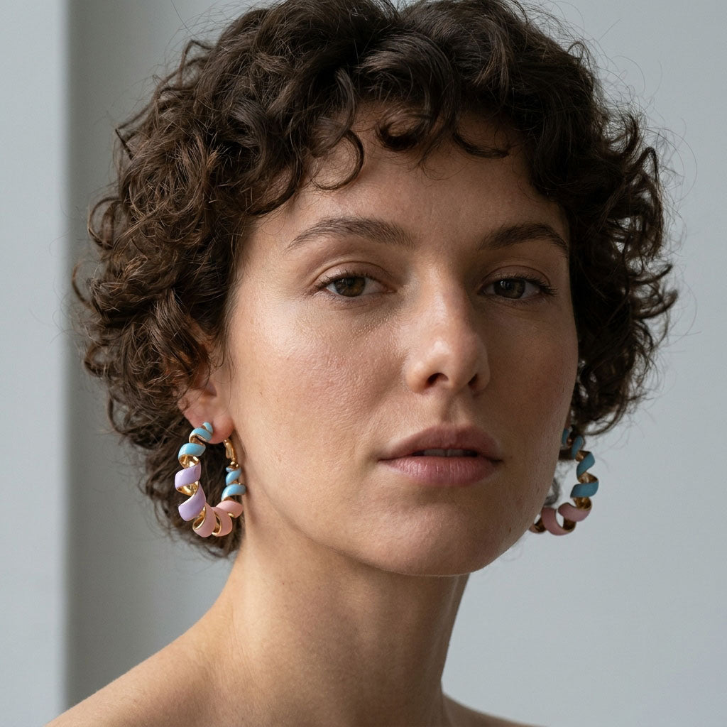 Model with curly hair wearing pastel enamel spiral earrings in gold tone