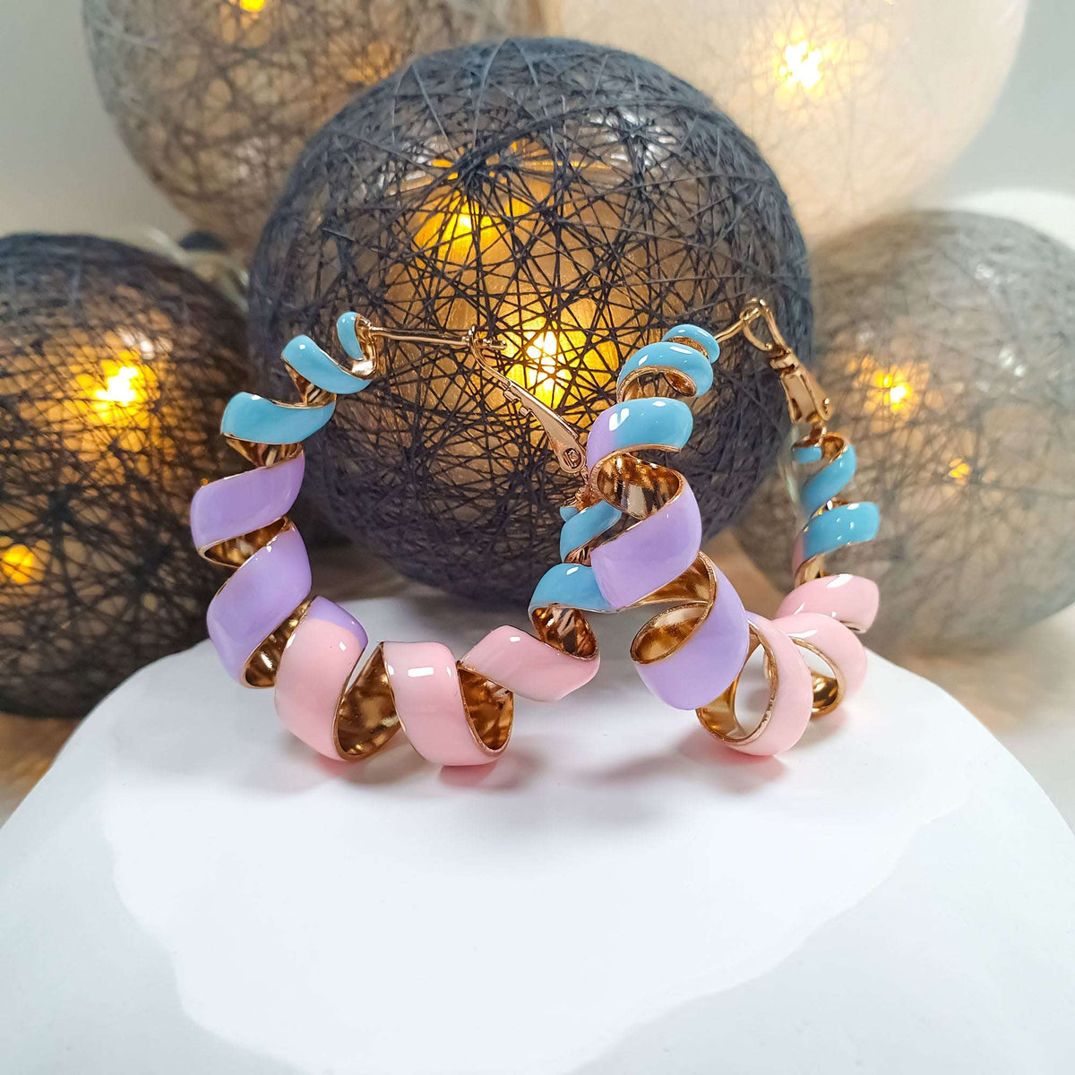 Gold-plated spiral earrings close up on a white stand with warm lights behind