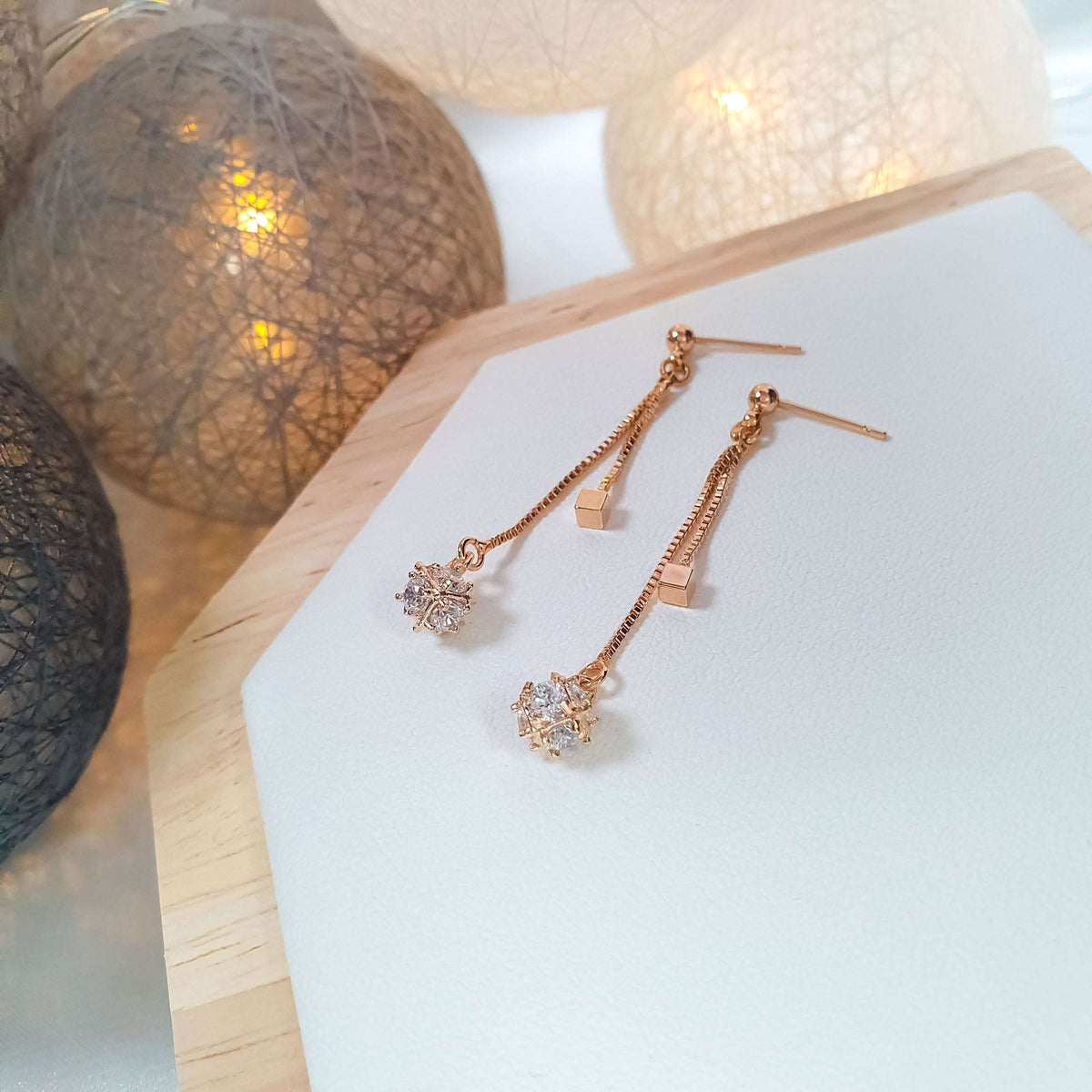 Chain drop earrings with clear stones on a light wooden stand