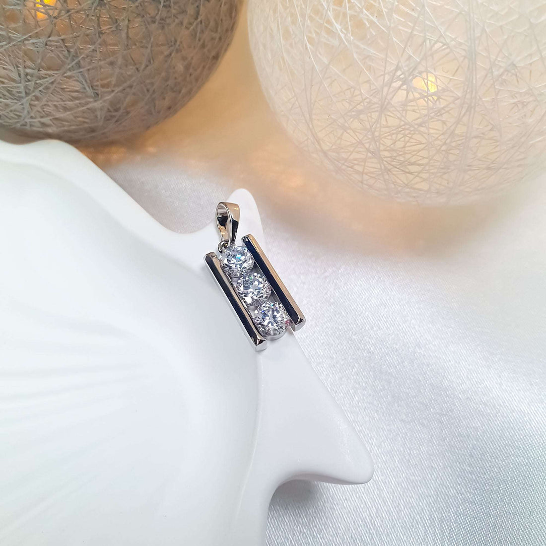 Silver-tone pendant with three sparkling stones at an angle on a ceramic stand