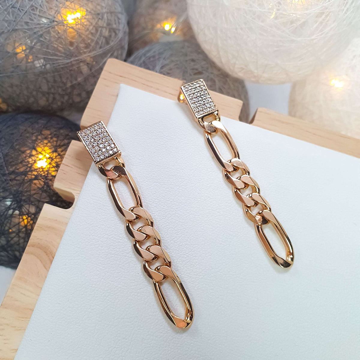 Two Figaro chain earrings with cubic zirconia rectangles on a white leather stand