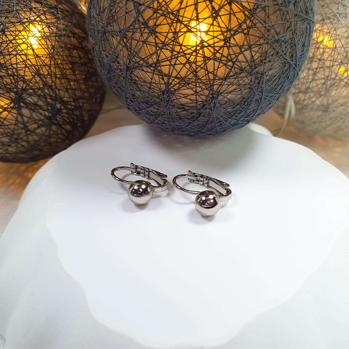 Silver-tone earrings with a smooth ball and French hooks on a white stand