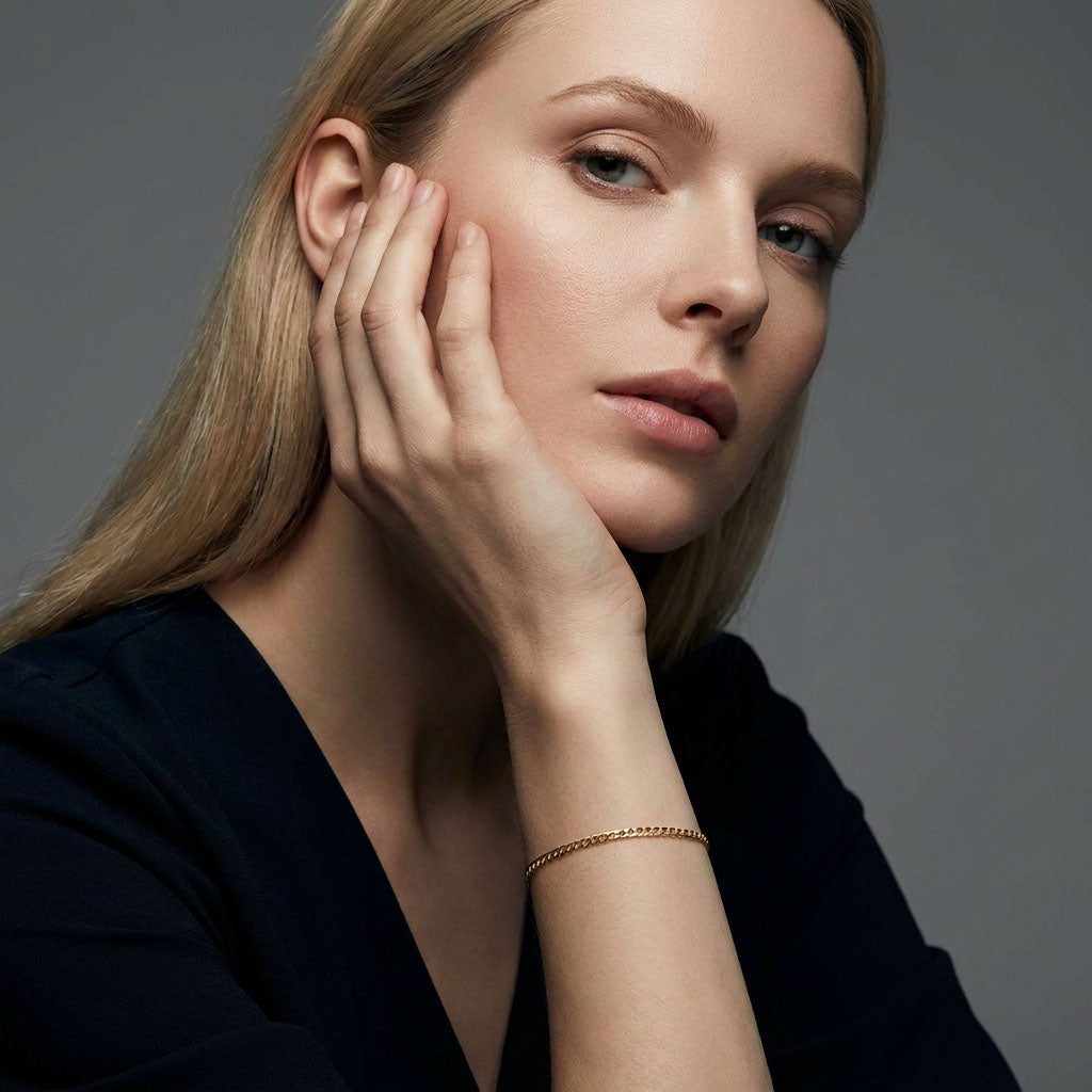 Model in a dark blouse wearing a fine gold-plated chain bracelet, grey background