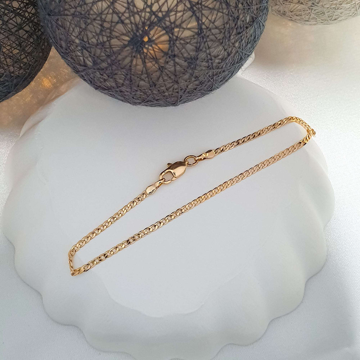 Fine gold-plated bracelet with a lobster clasp coiled on a white decorative plate