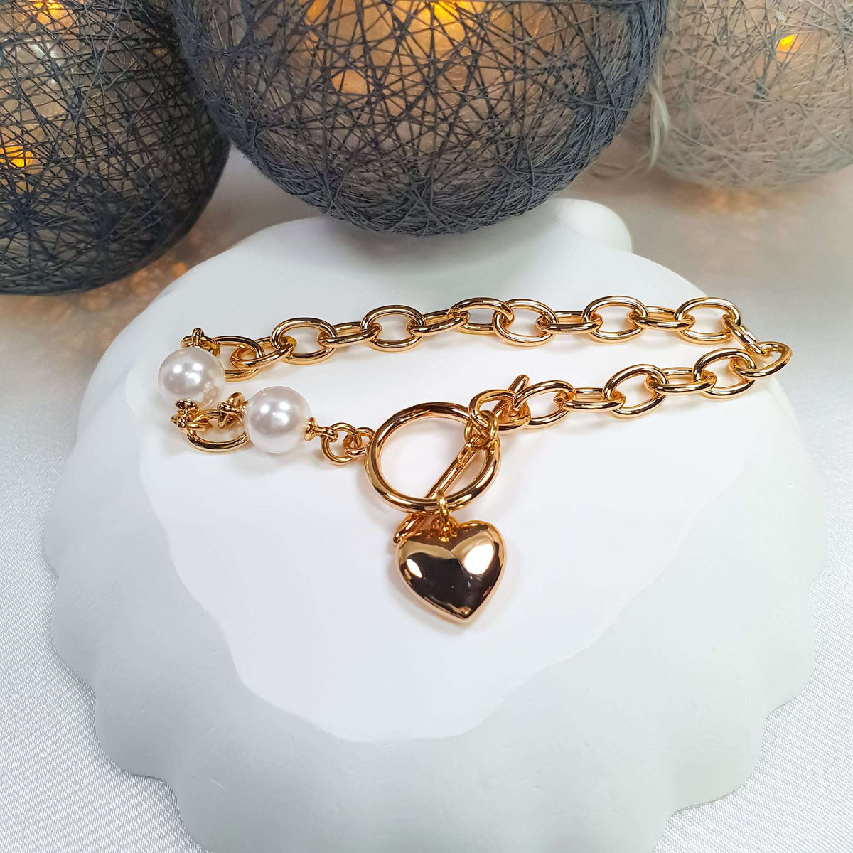 Gold-plated pearl bracelet with a heart charm on a white plate, festive setting