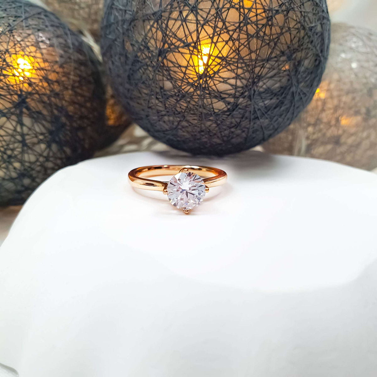 Gold-tone ring, round brilliant-cut cubic zirconia in a prong setting, glowing lights behind