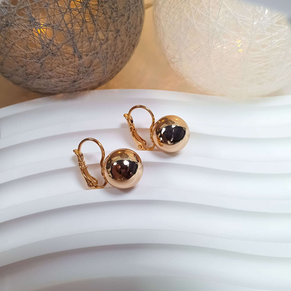 Gold-tone ball earrings on a white wavy stand in warm decorative light