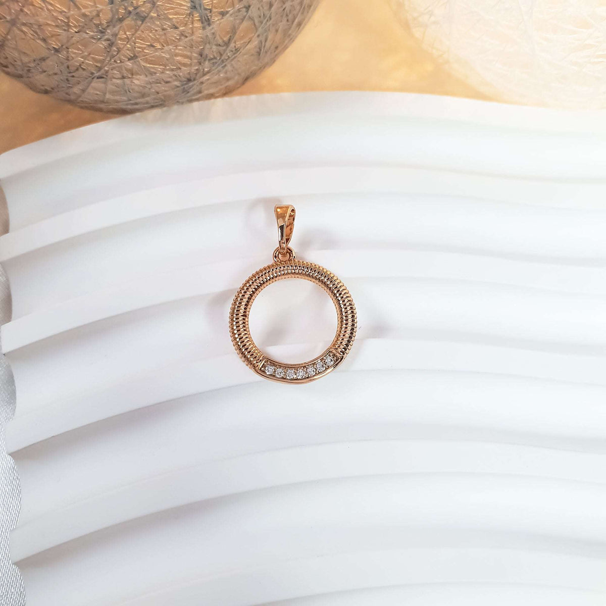 Ribbed round gold-tone pendant with a row of stones on a wavy surface