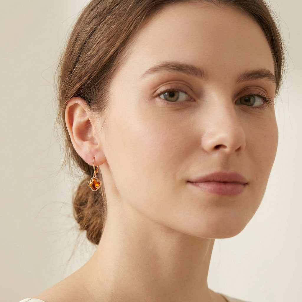 Gold-plated earring with an orange four-leaf stone on a model's ear, light background