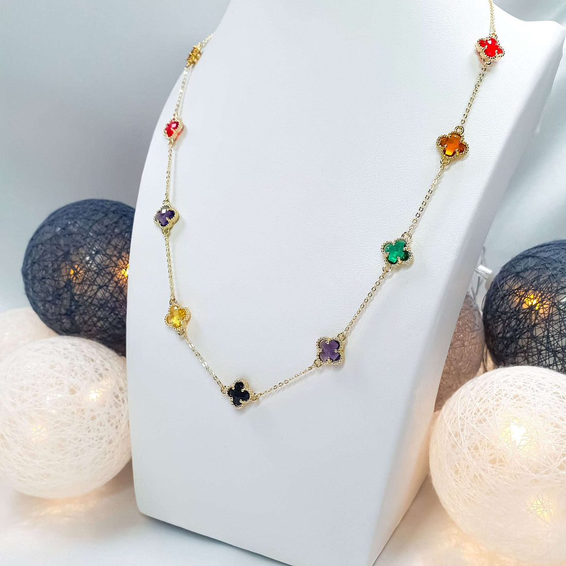 Multicoloured clover necklace on a white jewellery bust beside decorative lights
