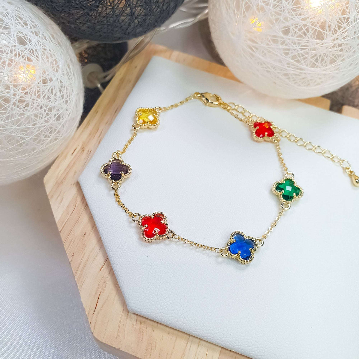 Colourful clover bracelet at an angle on a white stand, warm lights behind