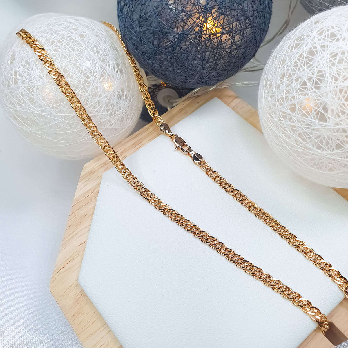 Gold-tone Nonna chain on a light jewellery stand among decorative lights