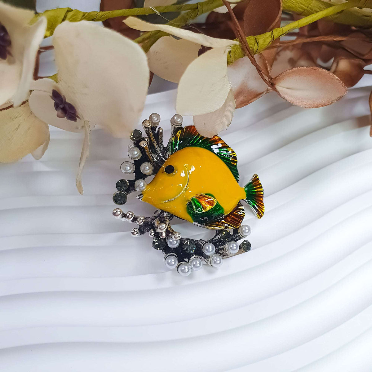 Fish brooch with pearl accents on a wavy background beside fabric flowers