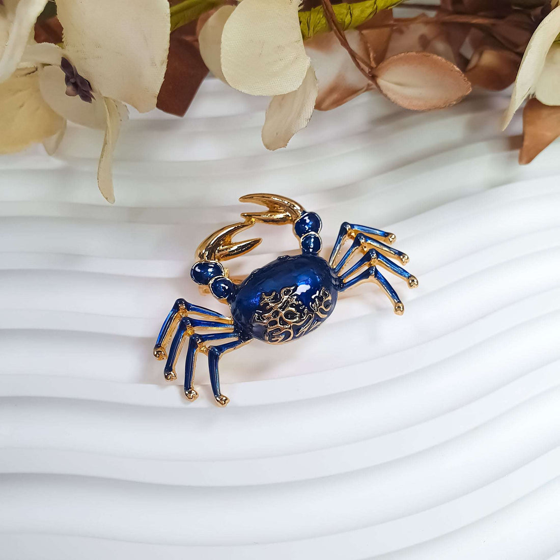 Blue enamel crab brooch with gold-plated claws on a light decorative surface