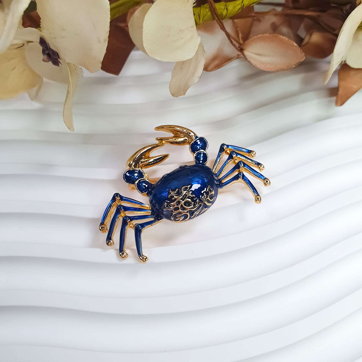 Blue enamel crab brooch with gold-plated claws on a light decorative surface