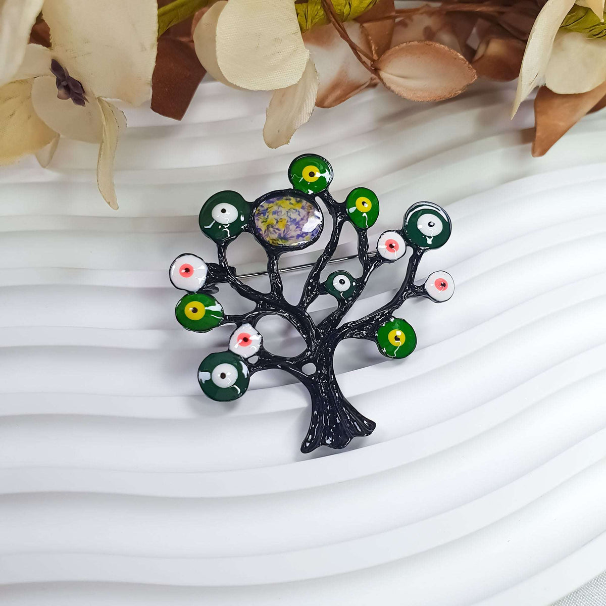 Tree of Life brooch at an angle among decorative flowers, green enamel circles
