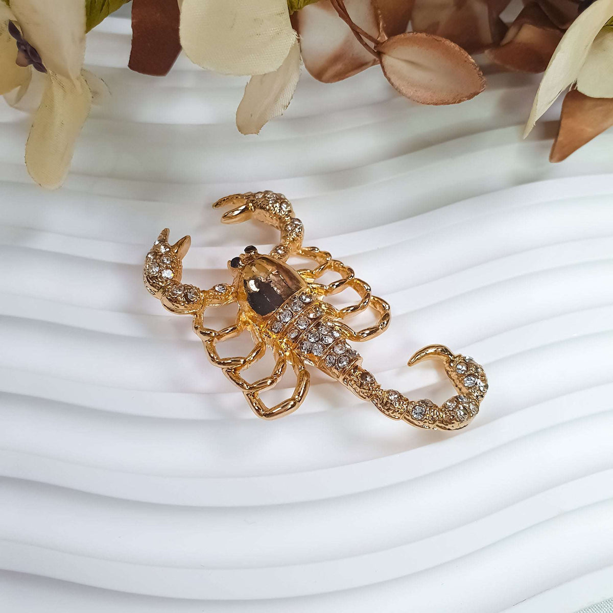 Scorpion brooch with a stone-covered tail and gold-tone body among flowers