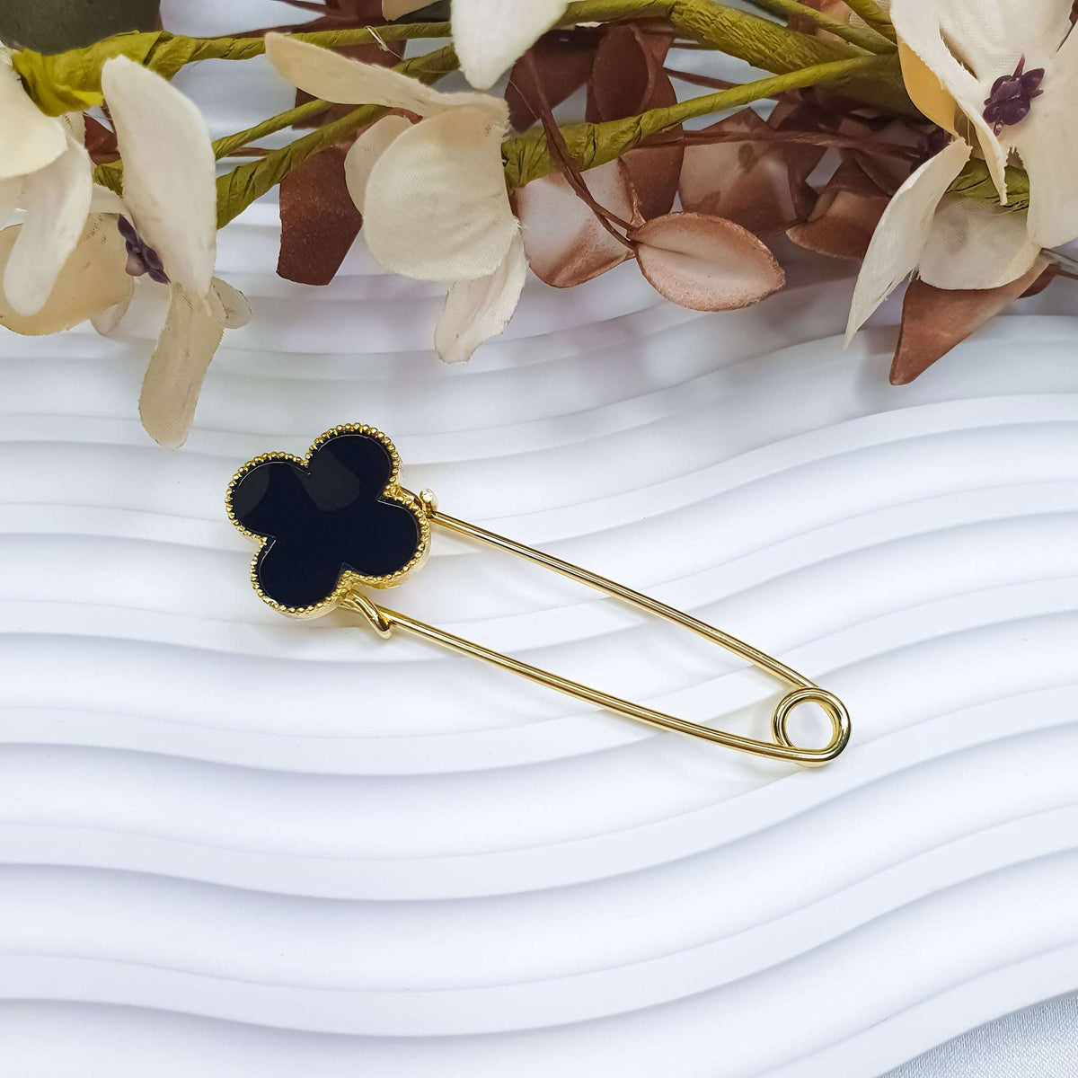 Four-leaf clover brooch in black enamel with a gold-tone safety pin on white