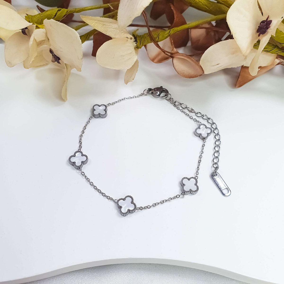 Platinum-plated white clover bracelet on a light background with decorative flowers