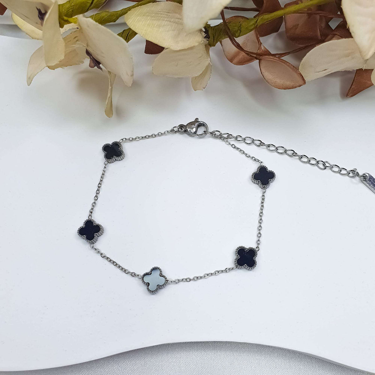 Adjustable black clover bracelet on a light background among decorative flowers